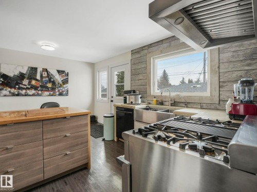Kitchen featuring a stainless steel range with a griddle, a large window with stone-look surround, a stainless steel double basin sink. - 7607 70 Avenue, Edmonton, AB 