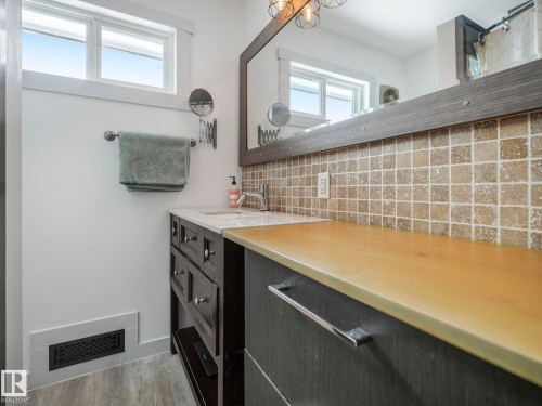 Bathroom featuring a vanity with a white countertop and rectangular sink, complemented by a tiled backsplash - 7607 70 Avenue, Edmonton, AB 
