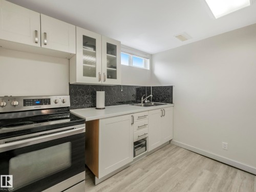Basement Kitchenette featuring white cabinetry, a stainless steel range, a single basin sink, white countertops. - 7607 70 Avenue, Edmonton, AB 