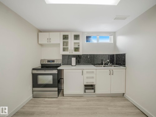 Basement compact kitchen area featuring white cabinetry, a stainless steel range, and a dual-basin sink - 7607 70 Avenue, Edmonton, AB 