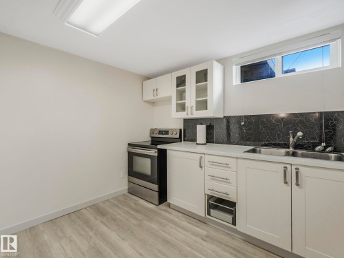 Basement kitchenette featuring with white cabinetry with brushed nickel hardware, and a stainless steel electric range - 7607 70 Avenue, Edmonton, AB 