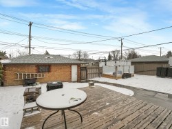 Expansive wood-finish deck with a patio table, accompanied by a brick garage with a shingle roof and a separate white door - 