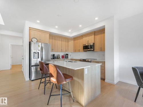 Contemporary kitchen featuring light wood-finish cabinetry, stainless steel appliances, a white subway tile backsplash, and a central island with a white countertop and seating - 4851 Kinney Road, Edmonton, AB - Indoor Photo Showing Kitchen