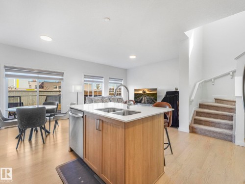Open-concept living area featuring a kitchen island with dual sinks and stainless steel appliances, wood-finish flooring, recessed lighting, and a carpeted staircase with a white railing - 4851 Kinney Road, Edmonton, AB - Indoor Photo Showing Kitchen With Double Sink