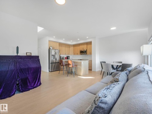 Open-concept living area featuring light wood-finish flooring, recessed lighting, and a modern kitchen with stainless steel appliances and light wood cabinetry - 4851 Kinney Road, Edmonton, AB - Indoor