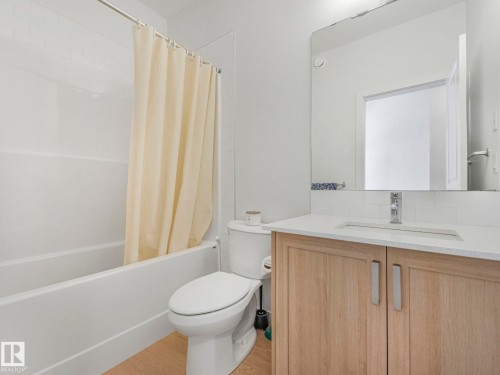 Bathroom with a built-in tub-shower combination, white subway tile surround, wood-finish vanity with panel doors, integrated sink, and a large unframed mirror - 4851 Kinney Road, Edmonton, AB - Indoor Photo Showing Bathroom