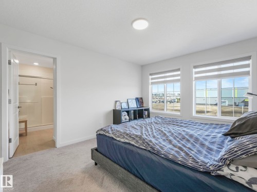 Carpeted room featuring dual windows with blinds, a ceiling-mounted light fixture, and a doorway opening to an en-suite with a glass-enclosed shower - 4851 Kinney Road, Edmonton, AB - Indoor Photo Showing Bedroom