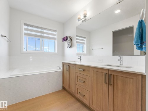 Bathroom featuring a built-in tub with subway tile surround, a dual vanity with light wood-finish cabinetry, white countertops, and chrome fixtures - 4851 Kinney Road, Edmonton, AB - Indoor Photo Showing Bathroom