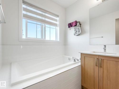 Built-in soaking tub with chrome fixtures, white subway tile surround, and a large window featuring a privacy blind - 4851 Kinney Road, Edmonton, AB - Indoor Photo Showing Bathroom
