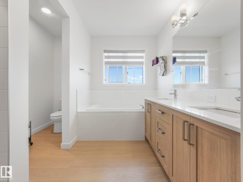 Spacious bathroom featuring a double vanity with light wood cabinetry, white countertops, and dual undermount sinks - 4851 Kinney Road, Edmonton, AB - Indoor Photo Showing Bathroom