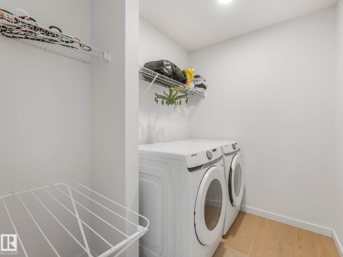 Dedicated laundry area featuring a front-load washer and dryer, practical wire shelving, and wood-finish flooring - 4851 Kinney Road, Edmonton, AB - Indoor Photo Showing Laundry Room