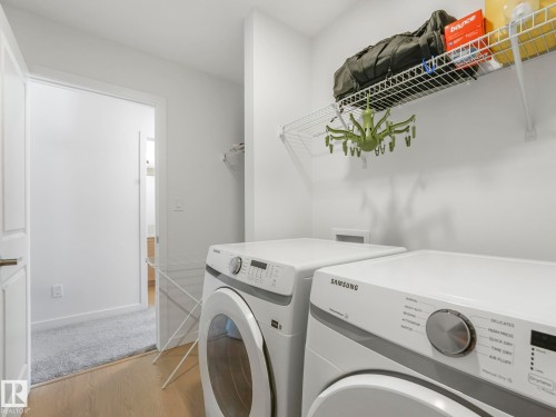 Dedicated laundry area featuring a front-loading washer and dryer, wood-finish flooring, white walls, and a wall-mounted wire shelving unit - 4851 Kinney Road, Edmonton, AB - Indoor Photo Showing Laundry Room