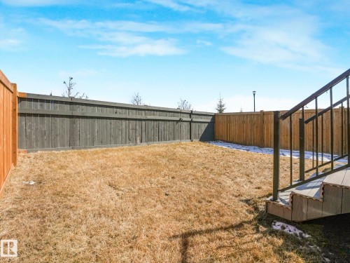 Fenced backyard featuring a wood deck with dark railings, a combination of natural wood and dark-stained wood fencing, and a lamp post visible in the distance - 4851 Kinney Road, Edmonton, AB - Outdoor
