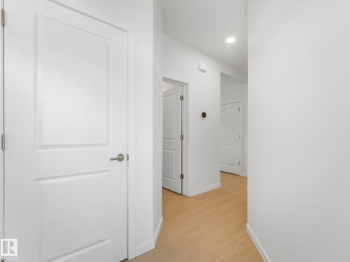 Hallway featuring light wood-finish flooring, white walls, recessed ceiling lighting, and multiple white paneled doors with brushed nickel hardware - 4851 Kinney Road, Edmonton, AB - Indoor Photo Showing Other Room