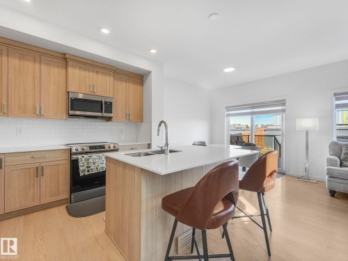 Open-concept kitchen featuring light wood-finish cabinetry, a stainless steel appliance suite, white subway tile backsplash, and light-toned countertops - 4851 Kinney Road, Edmonton, AB - Indoor Photo Showing Kitchen With Double Sink