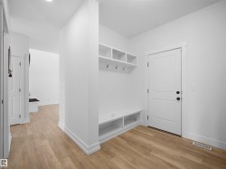 Entryway featuring light wood-style flooring, white walls, and built-in storage with shelves, hooks, and a bench - 