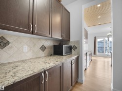 The kitchen features extensive cabinetry, a tiled backsplash with decorative accents, and a light-colored countertop - 