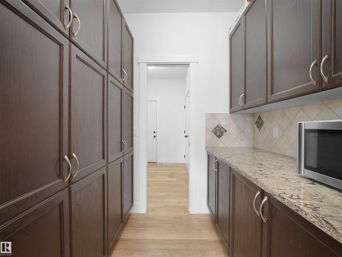 Well-appointed pantry featuring extensive dark wood cabinetry, light-colored countertops, and a tiled backsplash with decorative accents - 4231 Charles Close, Edmonton, AB - Indoor Photo Showing Kitchen