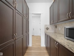 Well-appointed pantry featuring extensive dark wood cabinetry, light-colored countertops, and a tiled backsplash with decorative accents - 