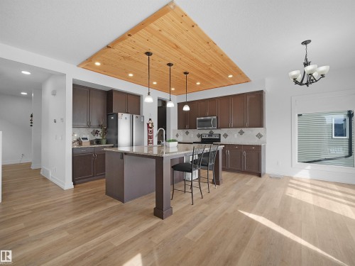 The kitchen features extensive cabinetry, a central island with bar seating, stainless steel appliances, and a tiled backsplash - 4231 Charles Close, Edmonton, AB - Indoor Photo Showing Kitchen With Upgraded Kitchen