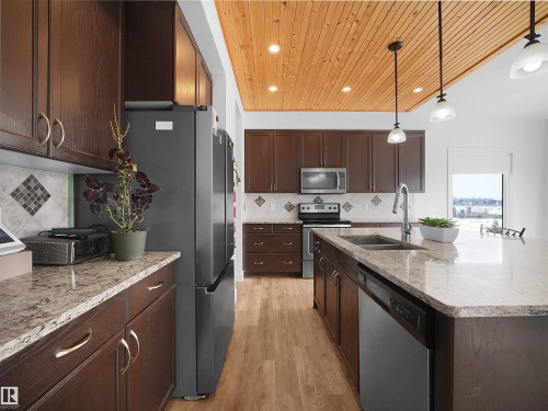 This kitchen features rich wood cabinetry, granite countertops, and a wood plank ceiling with recessed lighting and pendant lights - 4231 Charles Close, Edmonton, AB - Indoor Photo Showing Kitchen With Stainless Steel Kitchen With Double Sink With Upgraded Kitchen