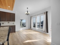 This bright and open room features light-toned flooring, a chandelier, and large windows with a view of a deck and railing - 
