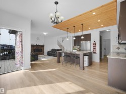 This open-concept living space features light wood flooring throughout, a kitchen island with seating, dark wood cabinetry, and stainless steel appliances - 