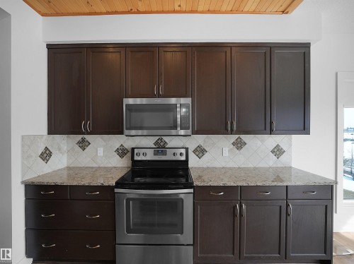 Kitchen featuring dark wood cabinetry, a stainless steel electric range, an over-the-range microwave, and granite countertops - 4231 Charles Close, Edmonton, AB - Indoor Photo Showing Kitchen