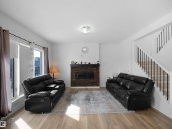 Living space featuring light-toned flooring, a stone-clad fireplace, and a staircase with white risers and dark balusters - 