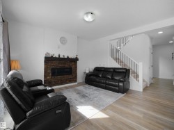 Inviting living space featuring light-colored flooring, a fireplace with a stone surround, and a staircase with white risers and dark banisters - 