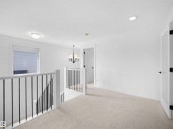 This property features a bright hallway with light-colored carpeting, a window with blinds, and white walls - 