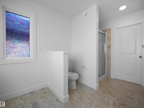 Bathroom featuring neutral-toned tile flooring, a window, a toilet, and a stand-up shower with a glass enclosure - 4231 Charles Close, Edmonton, AB - Indoor Photo Showing Bathroom