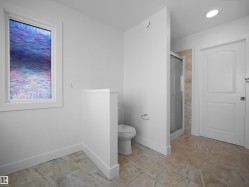 Bathroom featuring neutral-toned tile flooring, a window, a toilet, and a stand-up shower with a glass enclosure - 