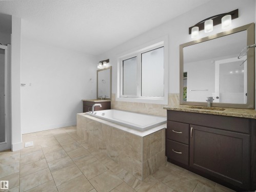 Bathroom featuring a built-in bathtub with tiled surround, a window with frosted glass, and two separate vanity areas with granite countertops and mirrors - 4231 Charles Close, Edmonton, AB - Indoor Photo Showing Bathroom
