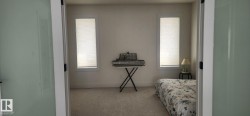 Bedroom featuring neutral-toned carpet flooring and two rectangular windows with cellular blinds - 