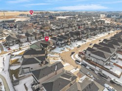 Aerial view of the neighborhood showcasing residential properties with grey roofs and varied exterior finishes, alongside a paved street and surrounding open land - 