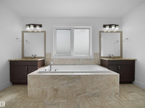 This bathroom features a spacious built-in bathtub with tiled surround, a window providing natural light, and two separate vanity areas with dark wood cabinetry, granite countertops, and mirrors illuminated by wall-mounted light fixtures - 4231 Charles Close, Edmonton, AB - Indoor Photo Showing Bathroom