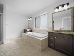 Bathroom featuring a built-in bathtub with tiled surround, a window with frosted glass, and two separate vanity areas with granite countertops and mirrors - 