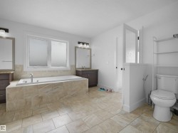 Spacious bathroom featuring large format tile flooring, a built-in bathtub with tiled surround, and two separate vanity areas with mirrors and lighting - 