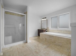 The bathroom features a spacious shower with sliding glass doors, a large bathtub with a tiled surround, and a vanity with a mirror and lighting fixture - 