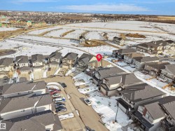 Aerial view showcasing the property within a residential development, featuring a mix of detached homes and townhomes, and proximity to undeveloped land - 