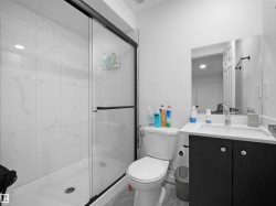 Bathroom featuring a glass-enclosed shower with white tiled walls, a white vanity with a dark cabinet, and a wall-mounted mirror - 