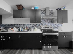 The kitchen features dark cabinetry, white countertops, a mosaic tile backsplash, and stainless steel appliances including a range and range hood - 