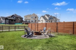 Expansive backyard featuring a lush lawn, a circular gravel fire pit area, and a horizontal plank privacy fence - 