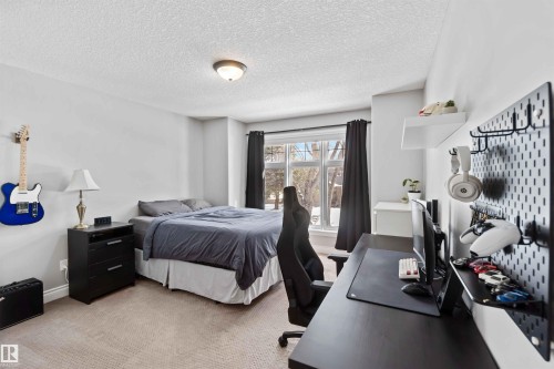 Spacious bedroom featuring neutral wall tones, carpet flooring, a large window with dark drapery, a flush-mount ceiling light, and a built-in wall shelf - 10630 82 Street, Edmonton, AB - Indoor Photo Showing Bedroom