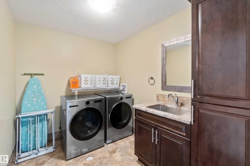 Dedicated laundry room featuring brown wood-finish cabinetry, a sink with a granite countertop, and tile flooring - 10630 82 Street, Edmonton, AB - Indoor Photo Showing Laundry Room