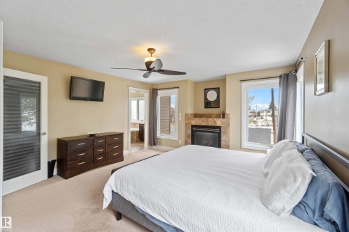 Carpeted room featuring a built-in fireplace with a stone surround, a ceiling fan with integrated lighting, and multiple windows - 10630 82 Street, Edmonton, AB - Indoor Photo Showing Bedroom