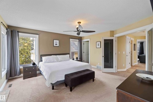 Carpeted bedroom featuring multiple windows, a ceiling fan with integrated lighting, and multiple paneled doors including one with frosted glass - 10630 82 Street, Edmonton, AB - Indoor Photo Showing Bedroom
