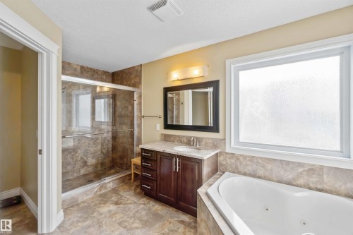 Spacious bathroom featuring a corner soaking tub, glass-enclosed shower with tiled walls, single vanity with countertop, and large frosted window - 10630 82 Street, Edmonton, AB - Indoor Photo Showing Bathroom