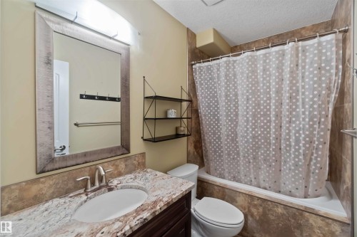 Bathroom featuring a vanity with a light-toned stone countertop, an undermount sink with a brushed nickel faucet, and a large framed mirror - 10630 82 Street, Edmonton, AB - Indoor Photo Showing Bathroom